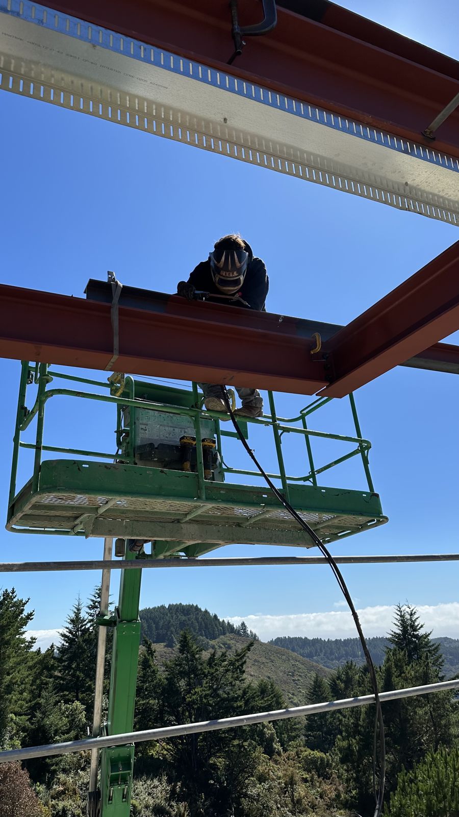 Welder working on an overhead steel beam from a lift