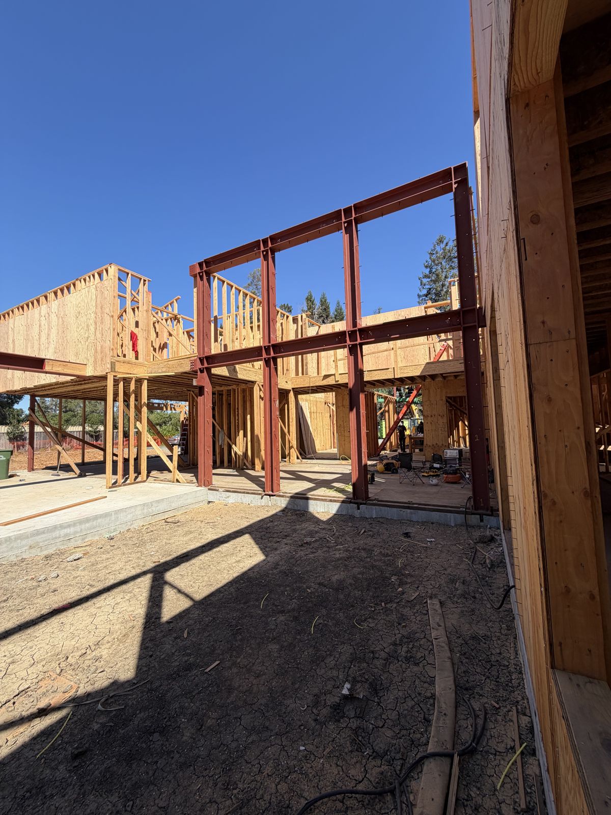 Red structural steel frame standing inside a wood-framed building under construction