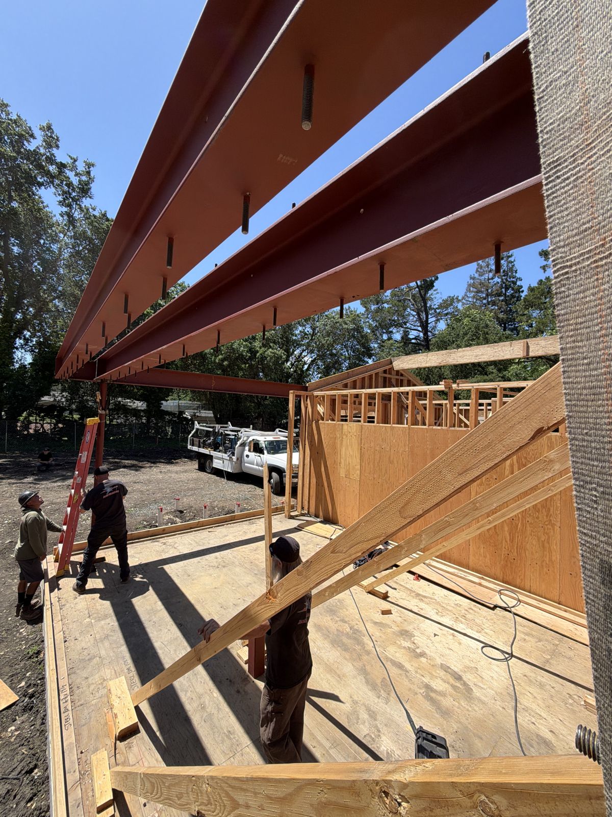 Steel beams installed overhead on a wood-framed building, with the crew working below