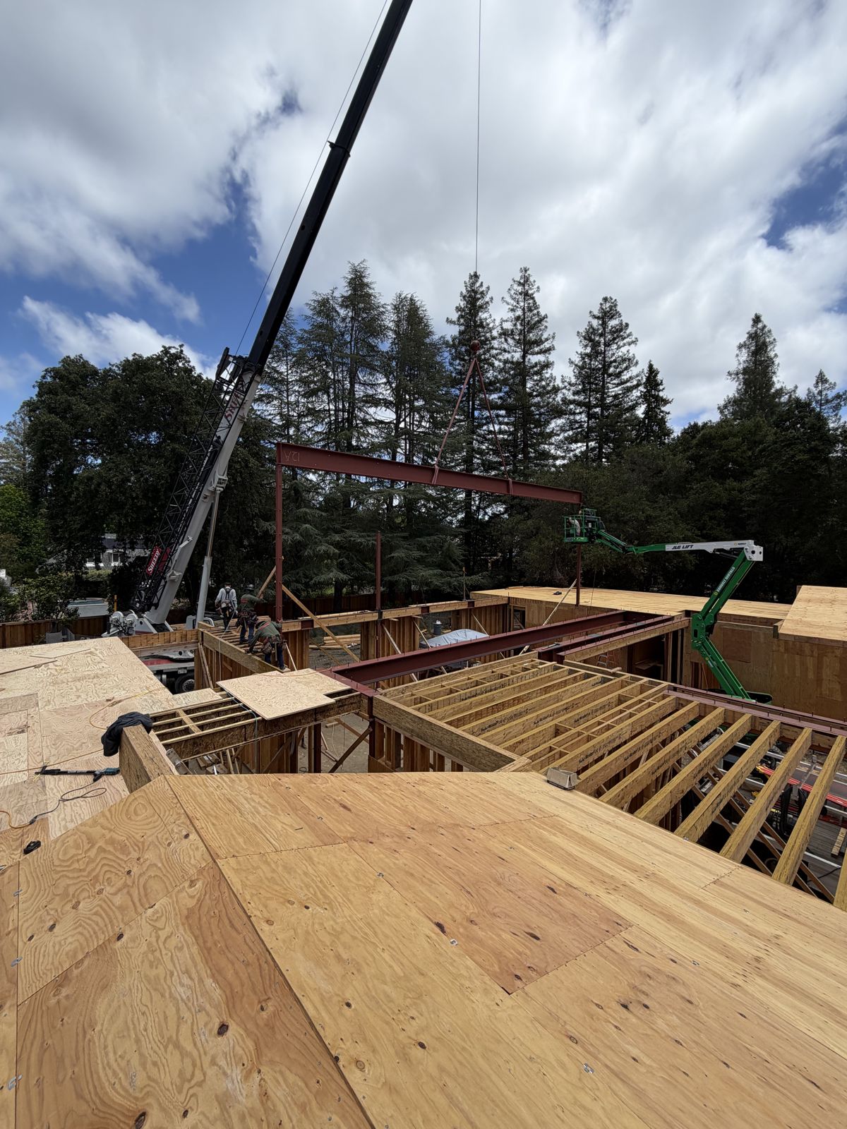 Crane lowering a steel beam onto a frame above a building under construction